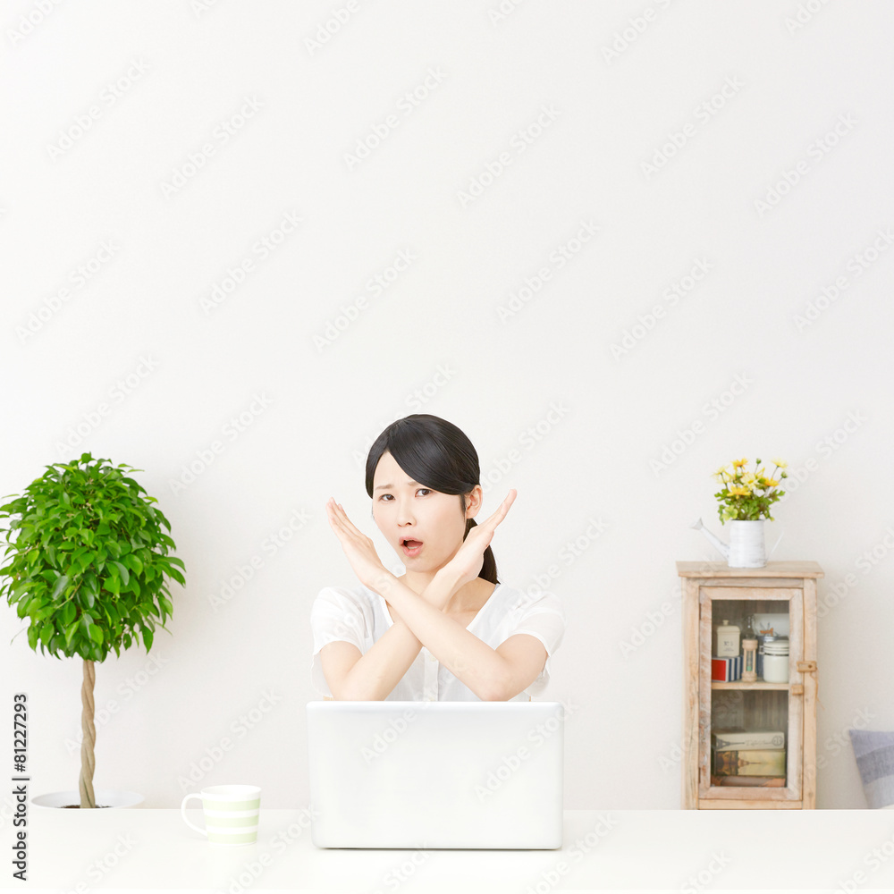 パソコンの前に座ってバツ印する女性