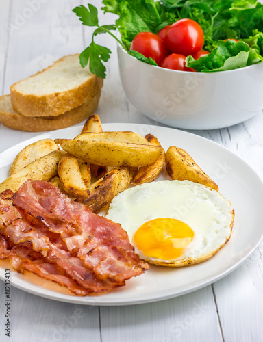 Hearty breakfast with bacon, fried egg, potato and vegetables