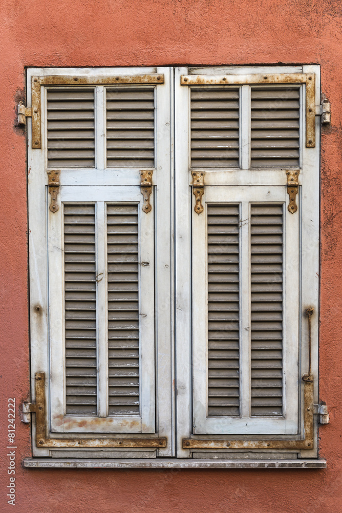 Closed white weathered window shutters on a red wall