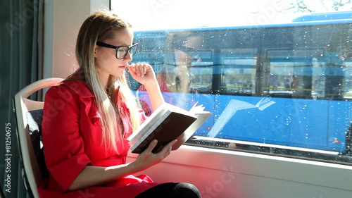 Blond young woman sitting in tram, reading book photo