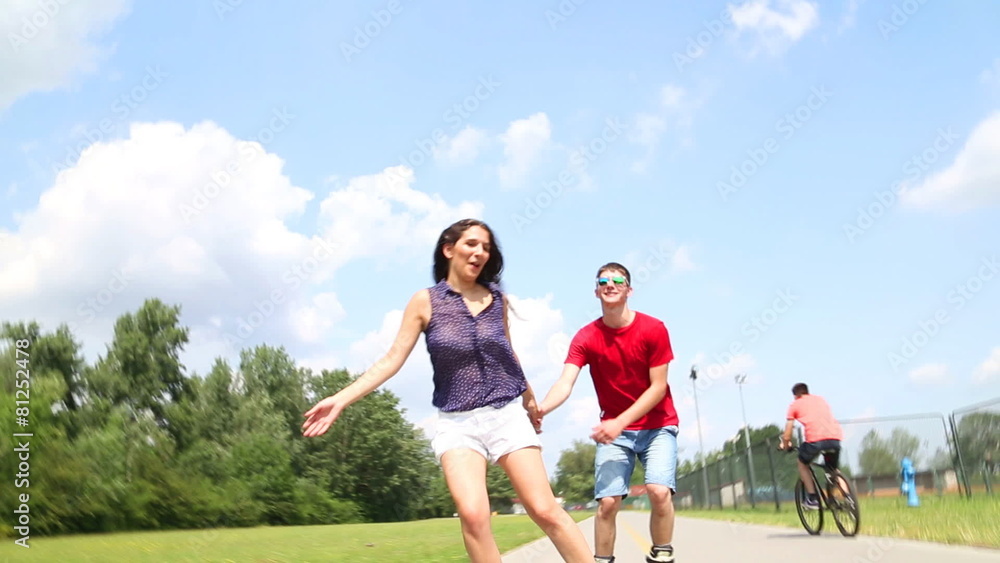 Young woman and man rollerblading on a beautiful sunny summer day in park, holding hands