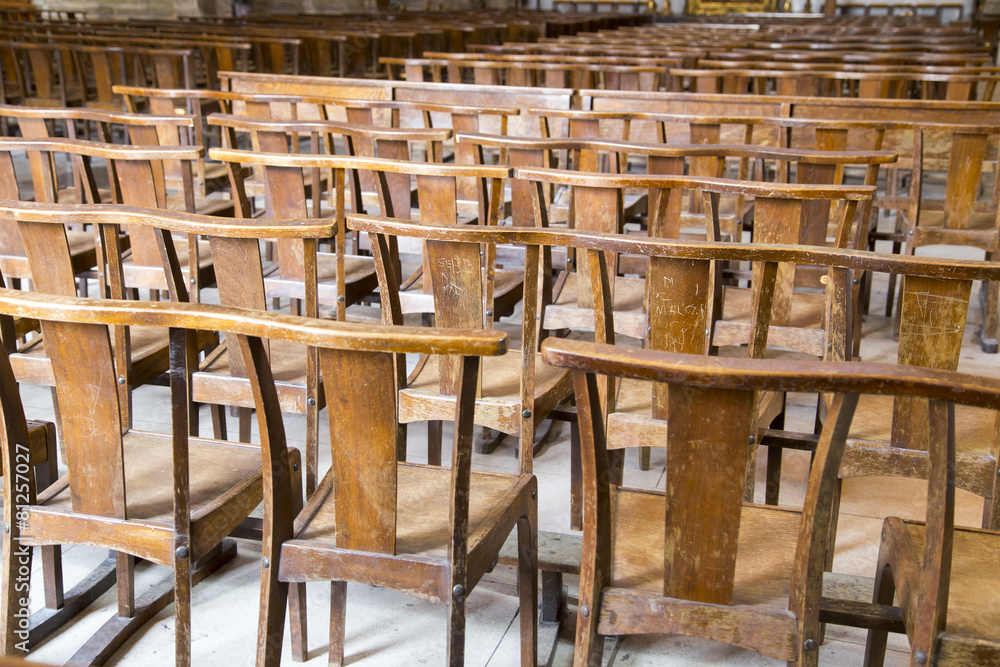 Rows of many worn wooden chairs in a church