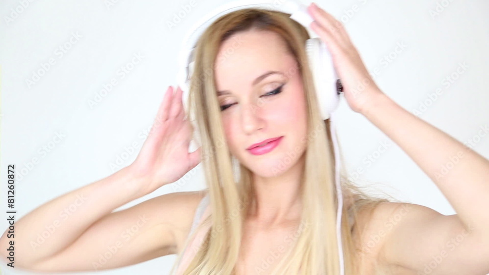 Beautiful young blond woman dancing with white headphones in white bright background Beautiful young blond woman dancing with white headphones in white bright background