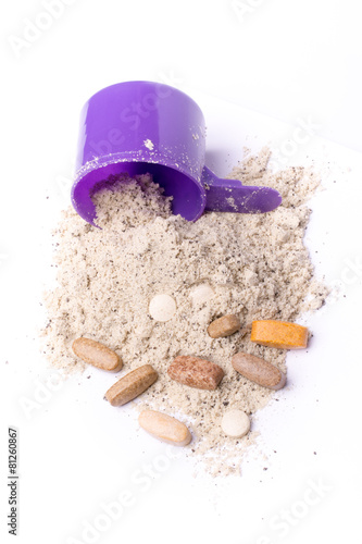 Whey protein powder in scoop with vitamins and plastic shaker on