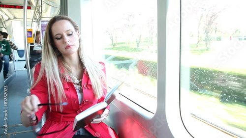 Beautiful young blond woman sitting in tram reading book and places her glasses photo