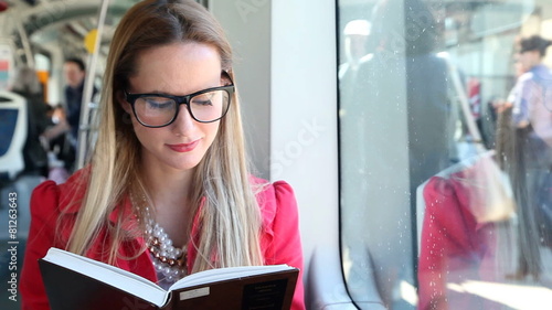 Cute blond woman reading book while driving in tram photo