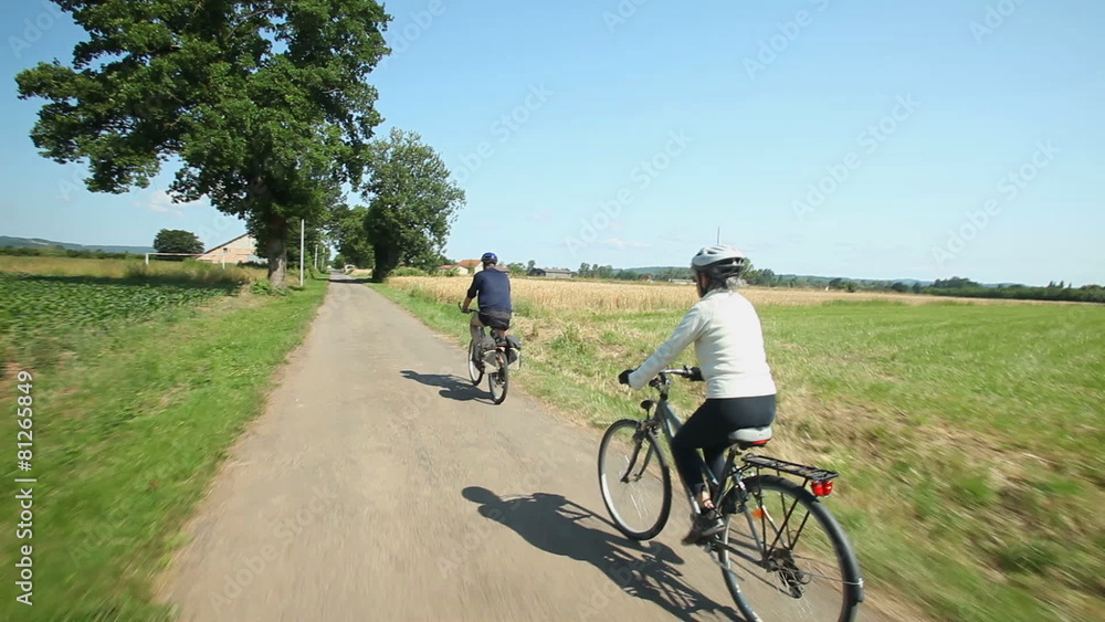 Retired couple cycling on road in village in France Retired couple cycling on road in village in France