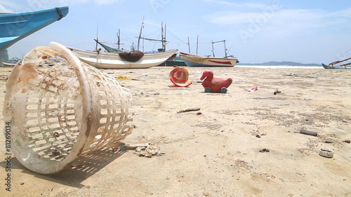 WELIGAMA, SRI LANKA - MARCH 2014: Trash washed up on shore in front of wooden fishing boast on beach. photo