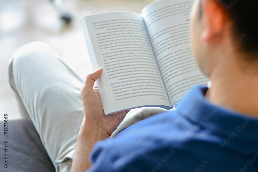 Fototapeta premium Young man reading book while sitting on the couch