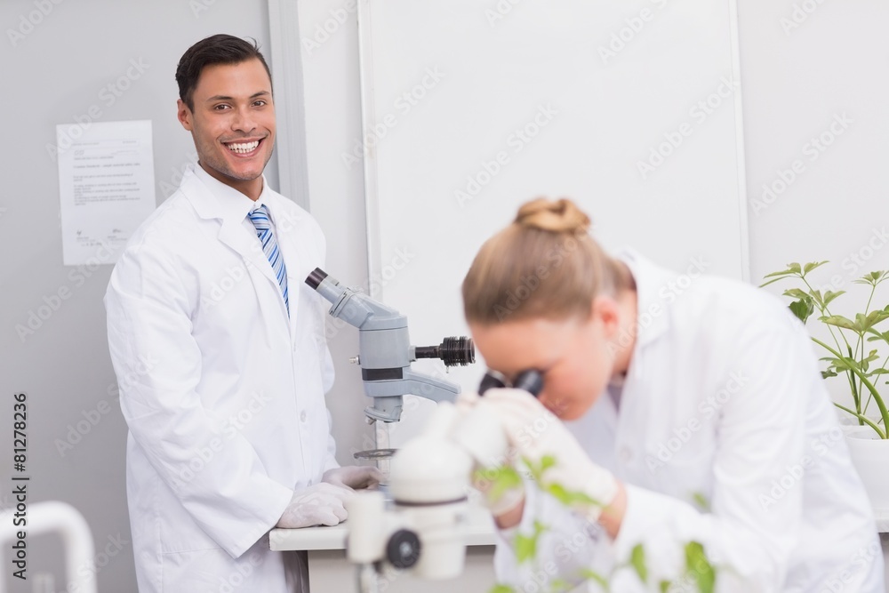 Happy scientist smiling at camera using microscope