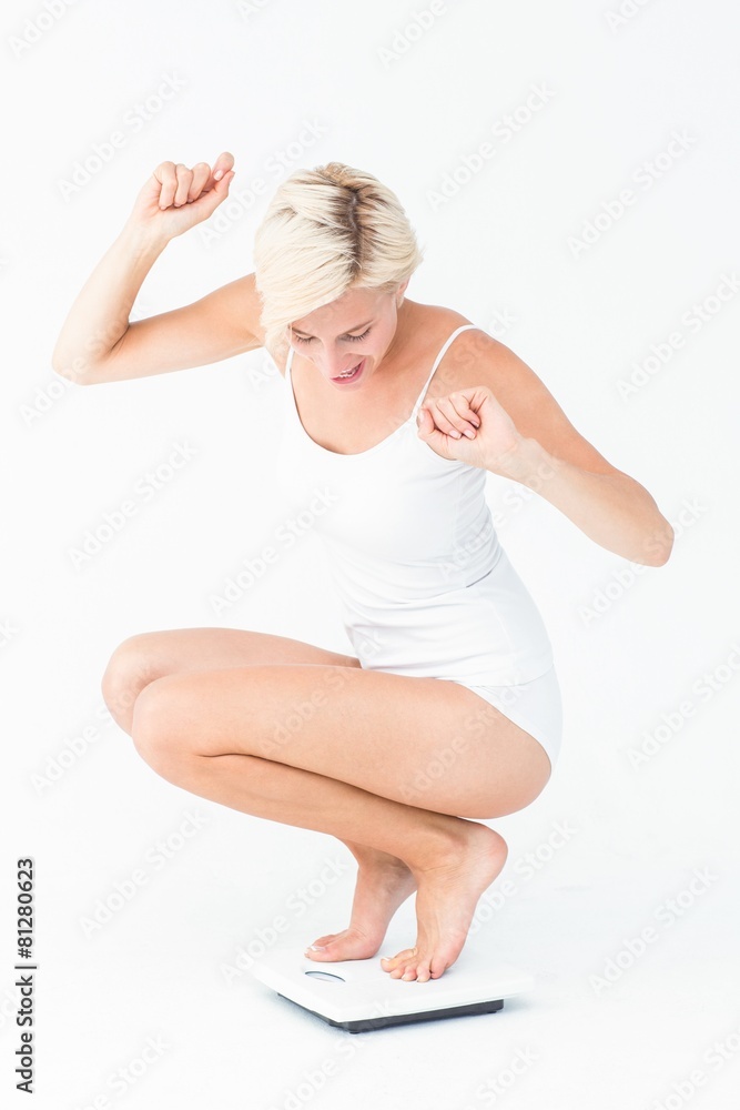 Happy attractive woman crouching on a scales Happy attractive woman crouching on a scales