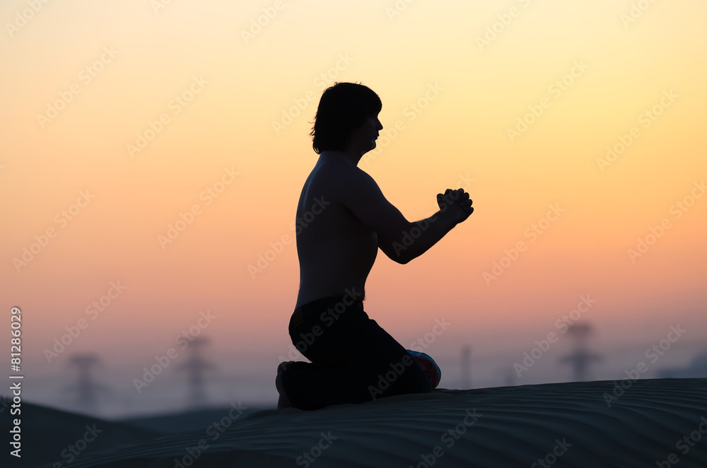Praying man silhouette staying on his knees alone in desert