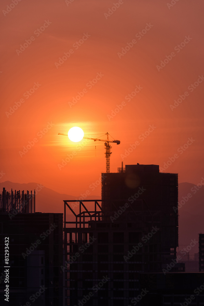 Industrial construction cranes and building silhouettes over sun Industrial construction cranes and building silhouettes over sun