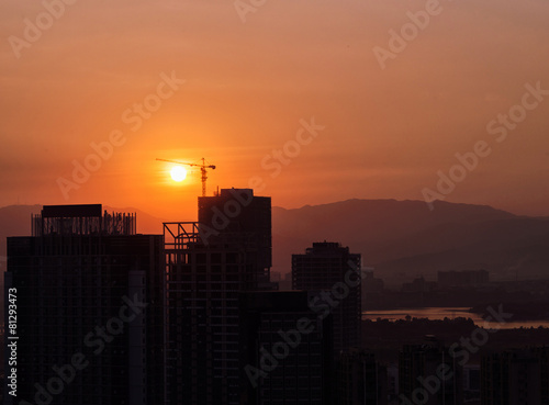 Industrial construction cranes and building silhouettes over sun