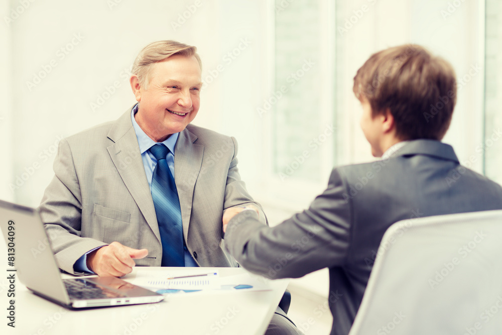 older man and young man shaking hands in office older man and young man shaking hands in office