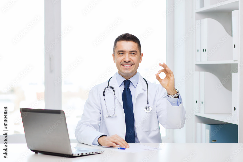 smiling doctor with laptop showing ok in office