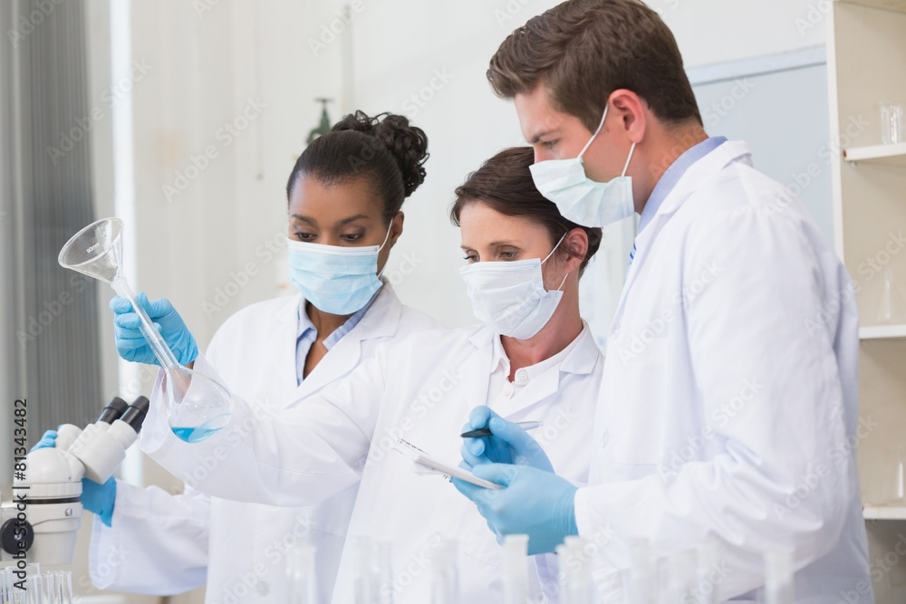 Scientists looking at beaker and taking notes Scientists looking at beaker and taking notes