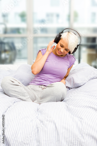 Blonde smiling woman is listening to music with headphones in th