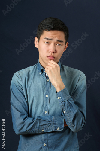 Pensive young Asian man looking at camera