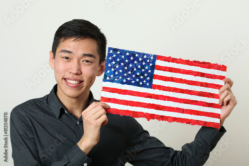 Young Asian student showing US national flag and looking at came