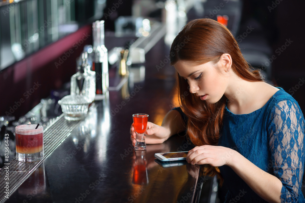 Young woman uses her phone in the bar