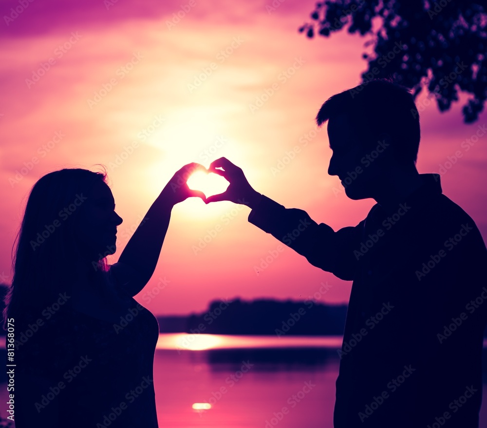 Couple doing heart shape with their hands on lake shore.