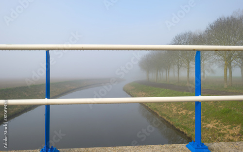 Blue white bridge railing over a foggy canal in spring