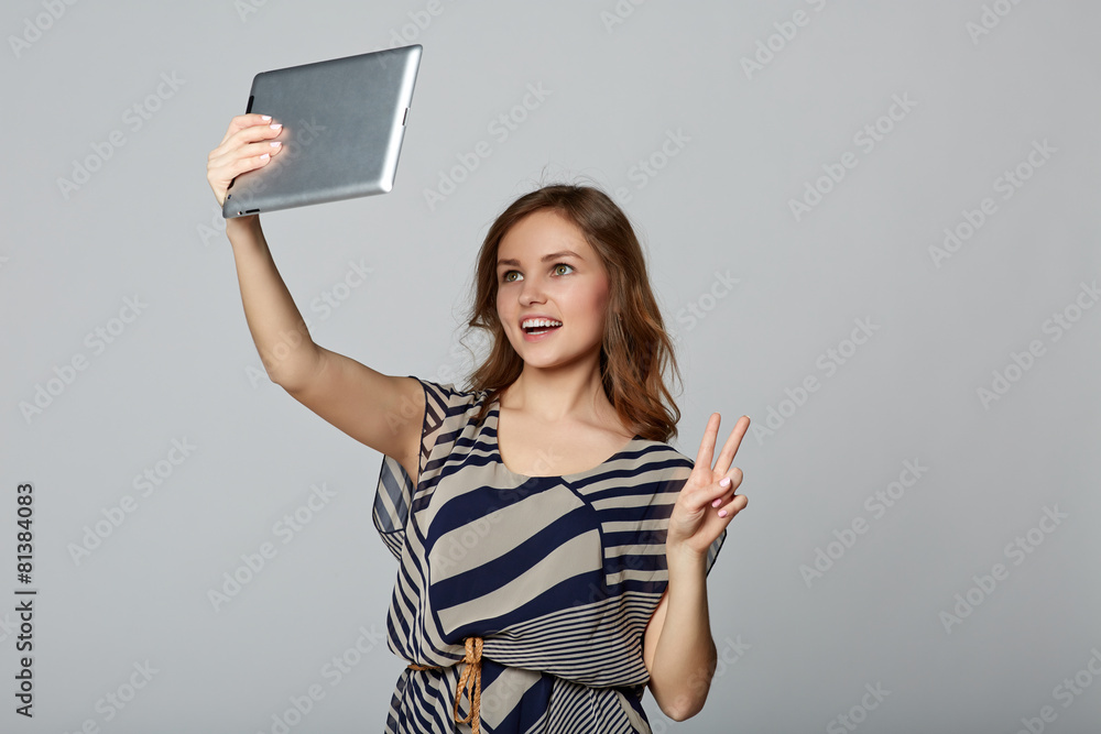Young woman taking selfie with digital tablet, on gray backgroun Young woman taking selfie with digital tablet, on gray backgroun