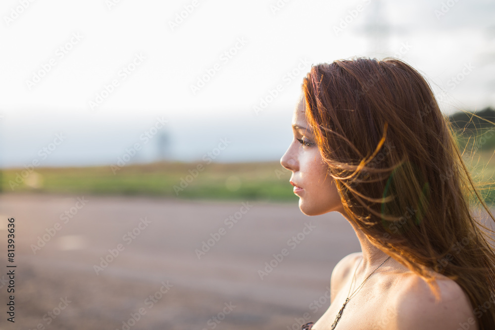 Red-haired young lady standing near the road at sunset Red-haired young lady standing near the road at sunset