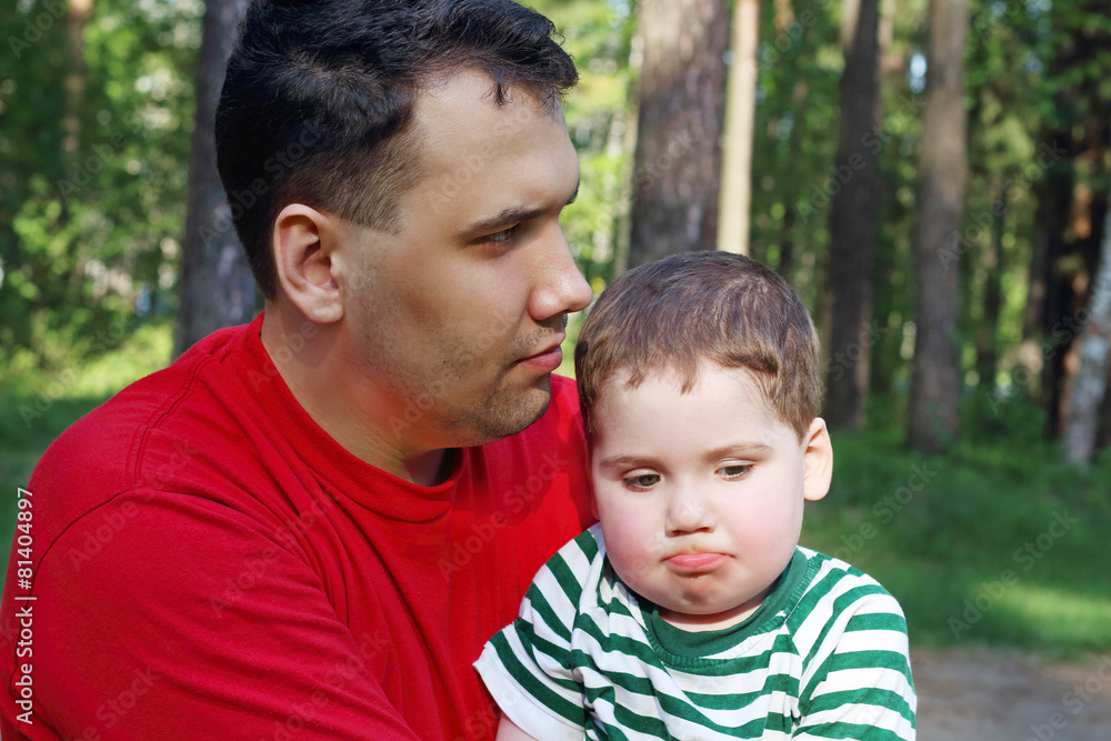 Handsome young father with little cute son sit in summer forest Handsome young father with little cute son sit in summer forest