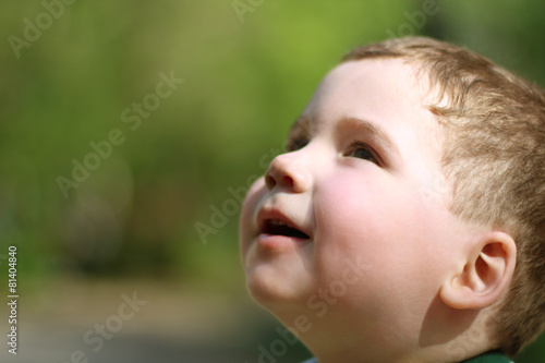 Smiling little cute boy looks up in park at summer day