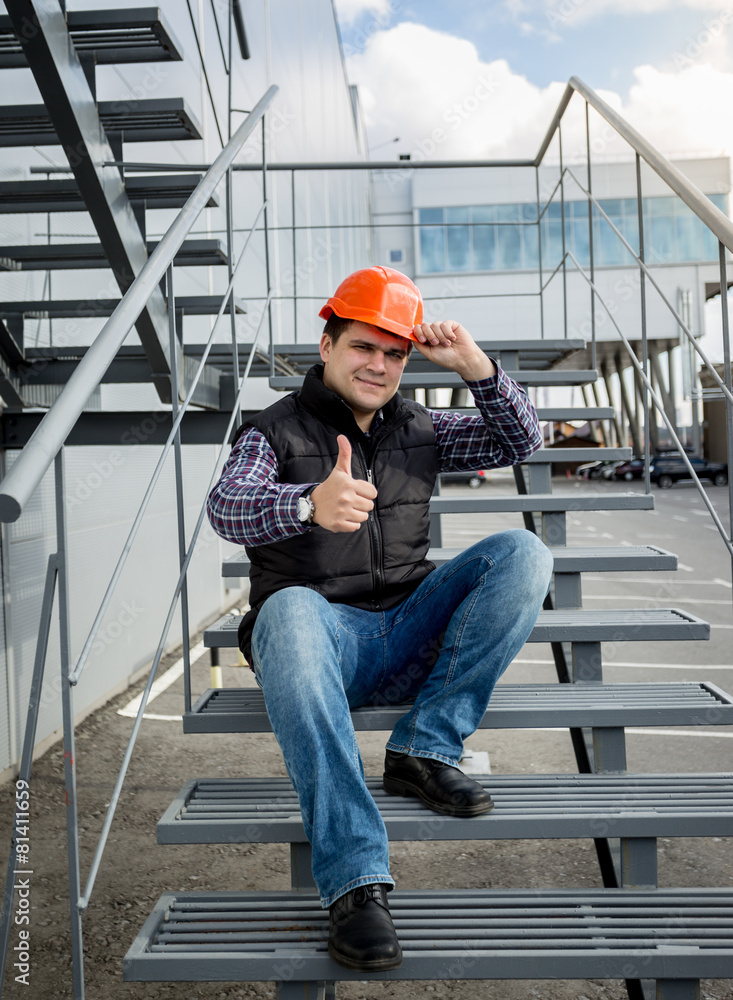 builder in helmet sitting on metal staircase and showing thumb u builder in helmet sitting on metal staircase and showing thumb u
