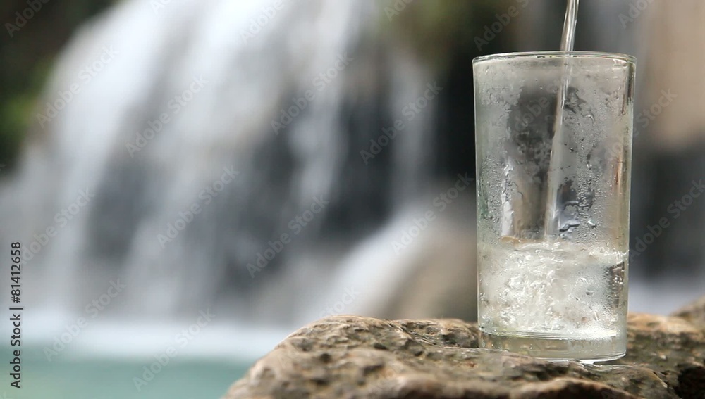 pouring water into a glass waterfall in the background pouring water into a glass waterfall in the background