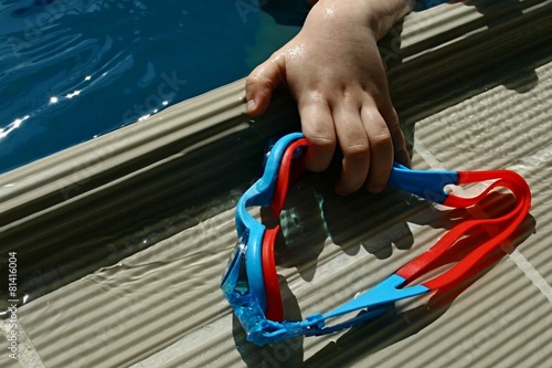Child hand grabbing children swim goggles from edge of pool