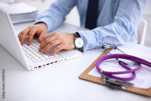 Male doctor using a laptop  sitting at his desk