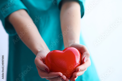 Female doctor with stethoscope holding heart over white