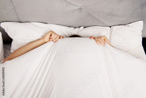 Man hiding in bed under sheets.