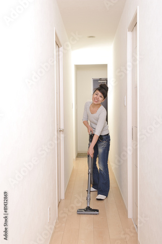 笑顔でマンションの部屋に掃除機をかけているアジア人の綺麗な女性
