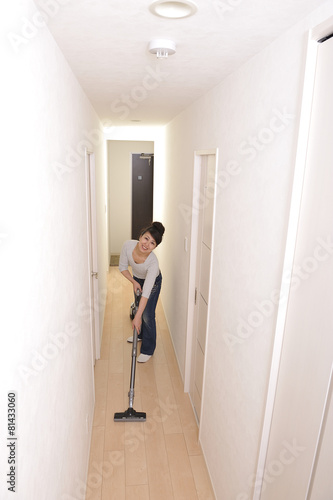 笑顔でマンションの部屋に掃除機をかけているアジア人の綺麗な女性 © beeboys