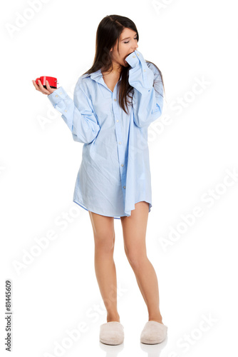 Young woman in big shirt holding alarm clock.