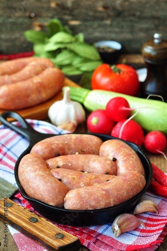 raw chicken sausages with vegetables on a frying pan