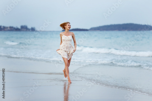A beautiful carefree girl is running along a sea shore at blue w