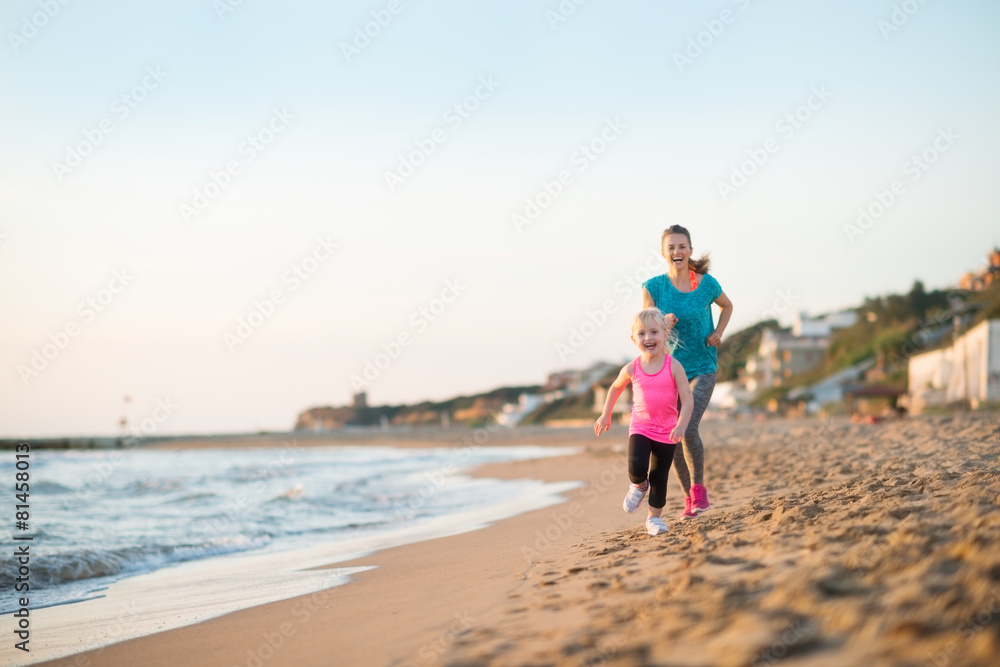 Healthy mother and baby girl running on beach in the evening