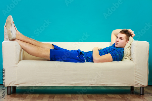 Young man relaxing on couch on blue