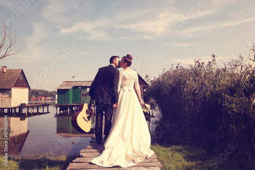 Bride and groom holding hands on bridge near lake houses