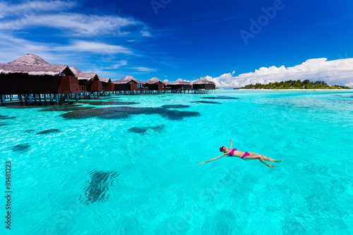 Young woman swimming from hut in tropical lagoon