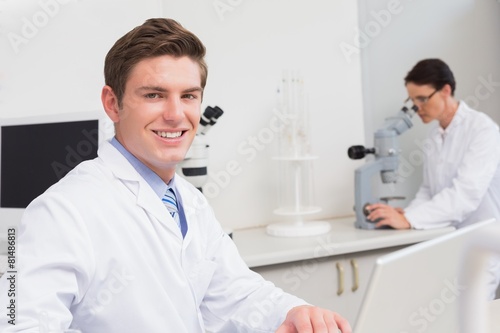 Scientist working with laptop and another with microscope
