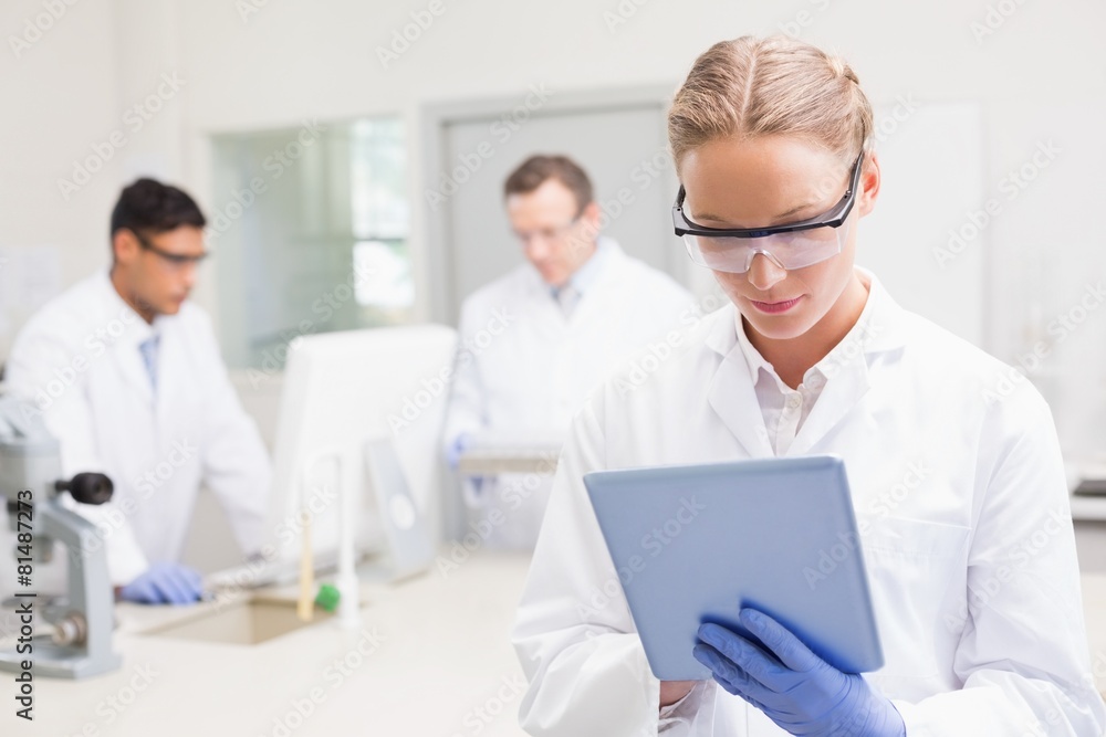 Scientist using tablet while colleagues working behind Scientist using tablet while colleagues working behind
