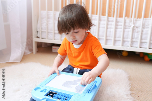2 years child in orange t-shirt paints on magnetic tablet at hom