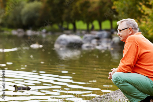 Mature man crouching near pond